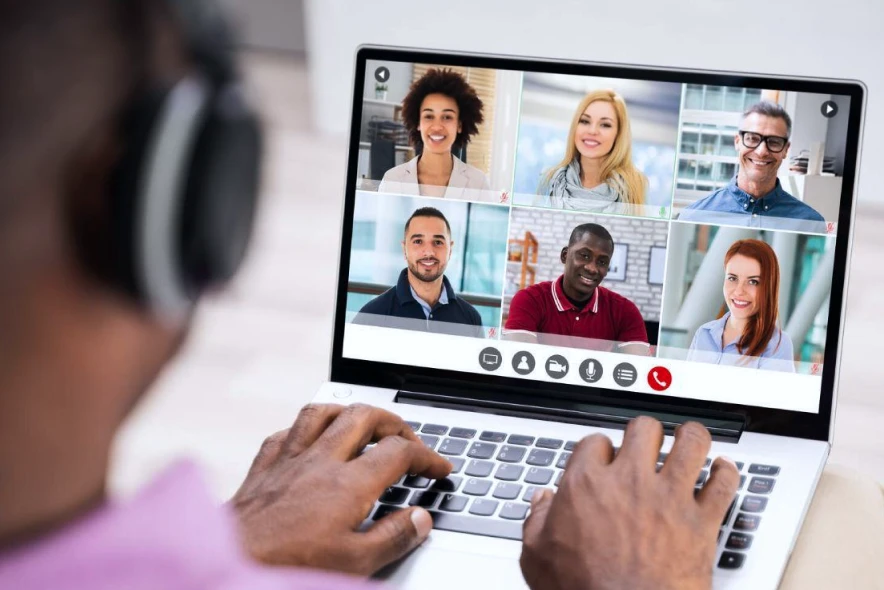 Person using a laptop for a video conference call with six colleagues, showcasing remote communication through an online meeting platform.