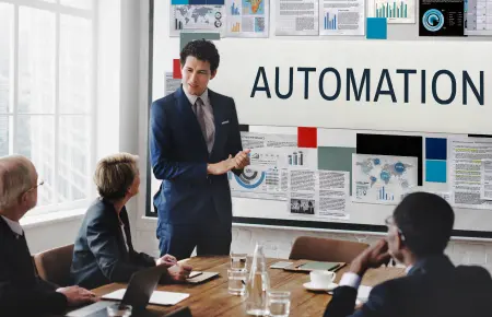 business meeting discussing sales process automation. A man presents in front of a screen showing 'AUTOMATION' and data visualizations to a diverse group of professionals.