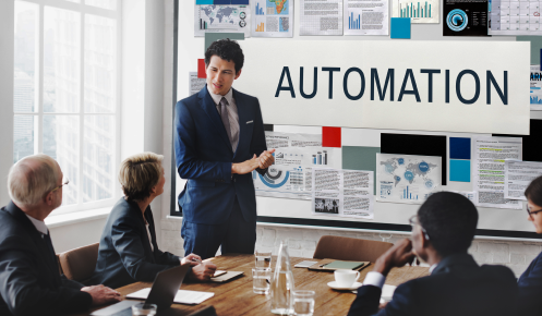 business meeting discussing sales process automation. A man presents in front of a screen showing 'AUTOMATION' and data visualizations to a diverse group of professionals.