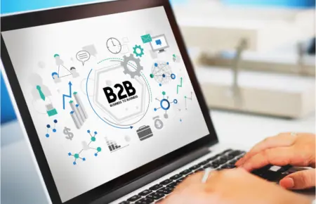 A person works on a laptop showing a graphic of the "B2B Business to Business" concept surrounded by icons