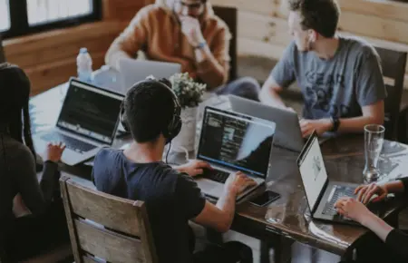 A group of young professionals working together on laptops in a collaborative workspace, discussing tech projects and digital tools like how to activate WhatsApp for business communication.